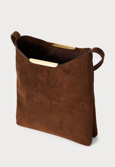Sac fourre-tout en suède brun avec une texture douce, ouverture sur le dessus, accents en fer doré, et deux poignées courtes pour un transport facile.