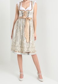 Robe dirndl avec un bustier blanc à volants et une jupe en satin beige ornée de motifs floraux en dentelle, accentuée par une ceinture en ruban assortie.