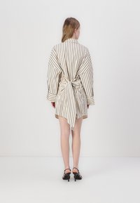 Dryžuota kimono stiliaus apsiaustu suknelė kreminiu ir juodu atspalviu, turinti raištį nugaros pusėje ir nevienodą apatinį kraštą, su plačiomis rankovėmis ir minkšta medžiaga.
