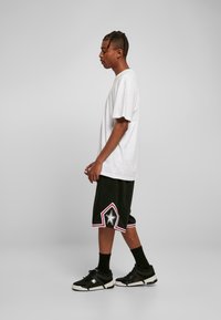 Biele tričko s krátkym rukávom, čierne šortky s červenými a bielymi hviezdami, a čierne tenisky s bielymi podrážkami, zobrazené z bočného pohľadu.