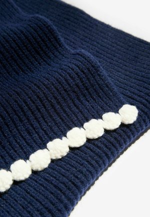 Tissu tricoté bleu marine avec un relief vertical, orné d'une bordure à pompons blancs, mettant en valeur la texture et les couleurs contrastées.