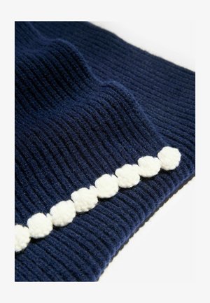 Tissu tricoté bleu marine avec un relief vertical, orné d'une bordure à pompons blancs, mettant en valeur la texture et les couleurs contrastées.