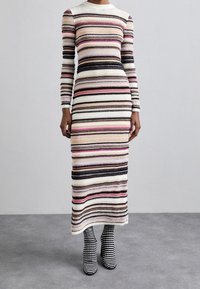 Lång, figurnära klänning med horisontella ränder i pastellfärger, svart och vitt. Har en rund halsringning och långa ärmar, kompletterad med randiga stövlar.