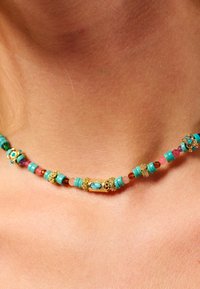 Collier en pierres turquoises avec des accents dorés, comprenant des perles rondes et cylindriques, entrecoupées de pierres orange et roses.