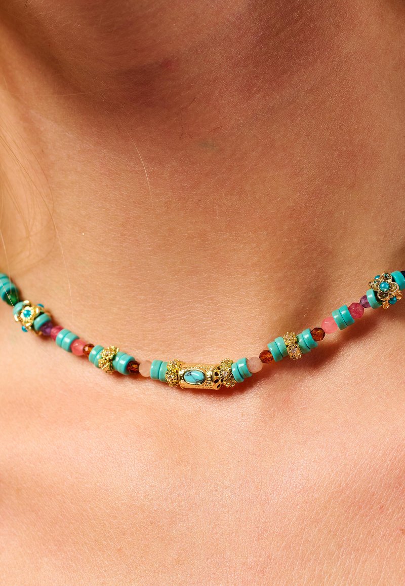 Collier en pierres turquoises avec des accents dorés, comprenant des perles rondes et cylindriques, entrecoupées de pierres orange et roses.