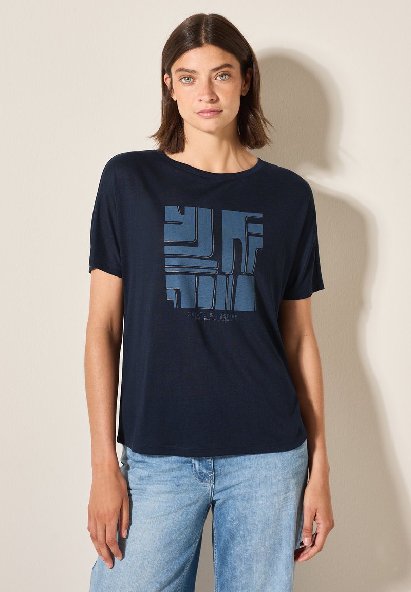 T-shirt à manches courtes bleu marine en tissu doux, avec un motif géométrique bleu et le texte "CRÉER & INSPIRER" en bas.