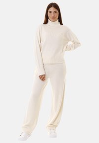 Maglione a collo alto di colore crema in maglia con orlo e polsini a costine, abbinato a pantaloni a gamba larga coordinati, realizzati in tessuto morbido.