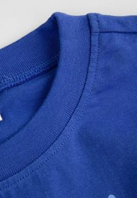 Niebieska bawełniana koszulka z okrągłym dekoltem. Gładka tekstura i jednolity kolor, z minimalnym przeszyciem wokół kołnierza.