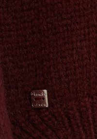 Tessuto a maglia rosso scuro con un piccolo bottone metallico quadrato cucito con filato rosso scuro, inciso con "Manila Grace".