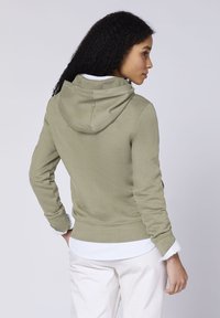 Olive green zip-up hoodie with a soft texture, featuring a hood and ribbed cuffs, layered over a white and blue striped blouse.