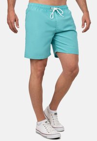 Pantaloni da bagno turchesi realizzati in tessuto leggero, dotati di una vita elastica con cordoncino bianco e un semplice dettaglio del logo.