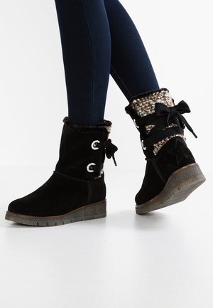 Czarne zimowe buty zamszowe z futrzanym obszyciem i dzianinowym mankietem, noszone z ciemnoniebieskimi obcisłymi dżinsami, pokazane z bocznego i tylnego kąta.