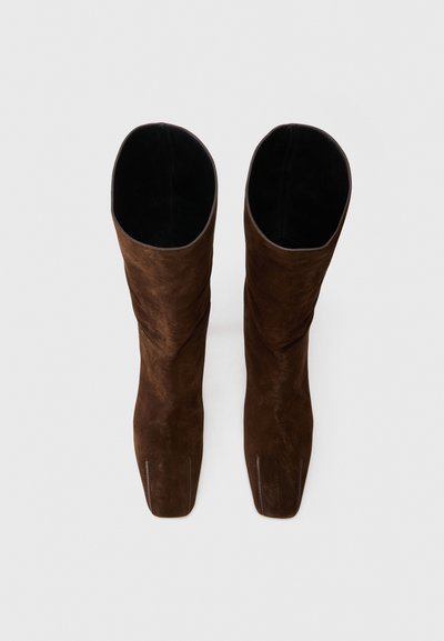 Stivali al ginocchio in suede marrone con una texture liscia, design angolare e apertura superiore, caratterizzati da una cucitura sottile lungo i lati.
