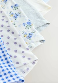 Des morceaux de tissu pliés avec des motifs vichy bleus, pois violets, petites fleurs bleues et gris clair uni disposés en chevauchement.
