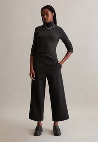 Black wide-leg trousers with a smooth texture, paired with a dark ribbed turtleneck sweater. Features a relaxed fit and ankle-length design.