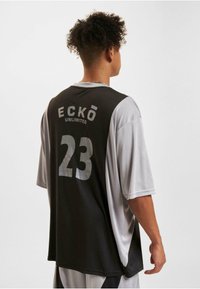 Maillot de basketball noir et gris à manches courtes. Présente le logo "ECKŌ UNLIMITED" et le numéro "23" au dos en matériau réfléchissant.