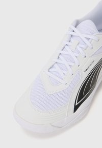 Baskets de sport blanches avec un tissu en maille, une semelle texturée, des lacets plats et un détail de conception noir contrastant sur le côté.