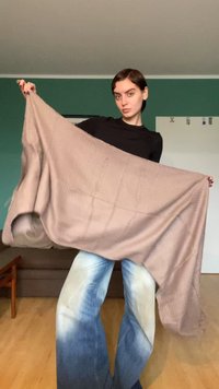 Écharpe en maille marron clair tenue ouverte, mettant en valeur une texture douce et un motif subtil. Le modèle porte un haut noir et un jean large bleu clair.