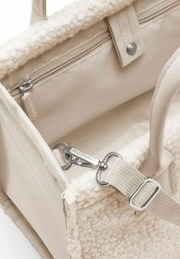 Borsa beige con un'esterno morbido e testurizzato, tasca interna con zip, ferramenta in argento e tracolla staccabile. Fodera liscia visibile.