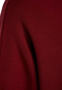 Gros plan sur un tissu en maille bordeaux montrant la texture du tissage et les détails de la couture.