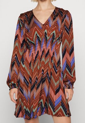 Sukienka z długim rękawem i dekoltem w serek, z wielokolorowym wzorem zygzaków w kolorach brązowym, czarnym, niebieskim, zielonym i białym na lekkiej tkaninie.