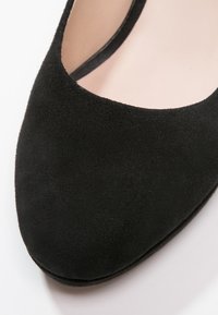 Gros plan d'une ballerine en daim noir à bout arrondi et empeigne basse sur fond clair.