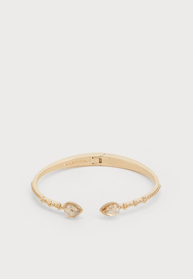 Pulsera de puño en tono dorado con una banda texturizada, que presenta dos cristales claros en forma de pera en cada extremo y detalles de cuentas a lo largo del lateral.