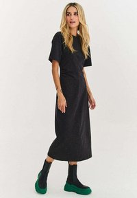 Mustast, lühikeste varrukatega midi-kleit, millel on tekstuuriga kangas koos värviliste laikudega. Sobitatud mustade ja roheliste platvormsaabastega.