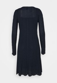 Robe en tricot bleu marine à manches longues avec motifs torsadés et ourlet festonné, vue de dos sur un fond uni.