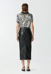 Srebrna kratka majica s paetama i crnim obrubom uparen s crnom kožnom midi suknjom koja ima prstenasti detalj na struku.