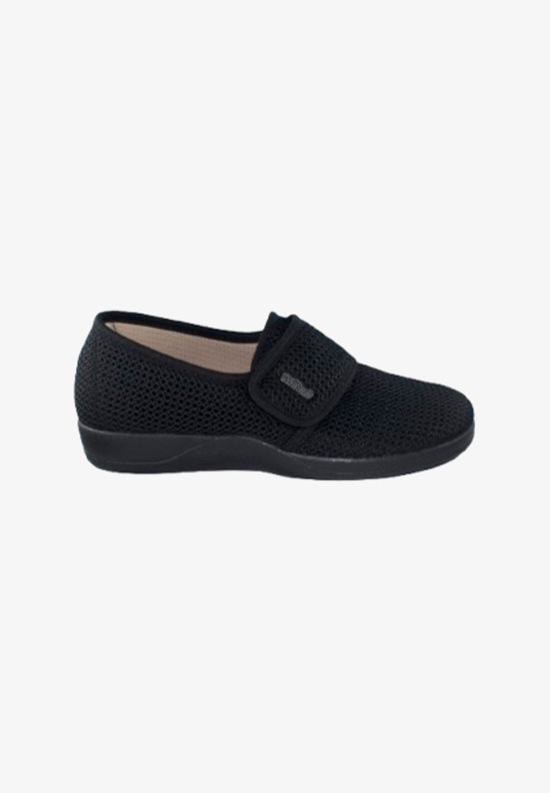 Zapato negro de malla tipo slip-on con una banda de Velcro. Cuenta con una suela de goma texturizada baja y un diseño de punta redondeada. El interior es beige.