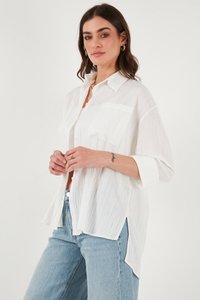 White, lightweight button-up shirt with a textured finish, side slits, and a chest pocket, paired with light blue jeans.
