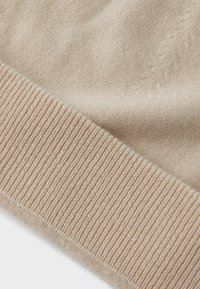Beige strikket stoff med en jevn tekstur og ribbestrikket kant. Fibrene ser myke ut, og det overordnede designet er enkelt og uten ornamenter.