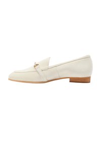 Loafers din suede bej cu un toc mic din lemn, având o curea decorativă din metal auriu în partea din față. Textură netedă, design minimalist.