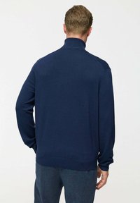 Sötétkék kötött pulóver magas nyakú, hosszú ujjas, bordás mandzsettával és aljjal. Simaság jellemzi, minimalista dizájn, minta vagy kiegészítők nélkül.