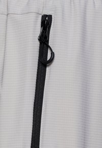 Black zipper with large pull-tab on light gray ripstop fabric textile.