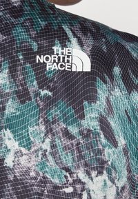 Chaqueta con patrón en verde oscuro y negro, con el logo blanco de "The North Face" en la parte superior de la espalda.