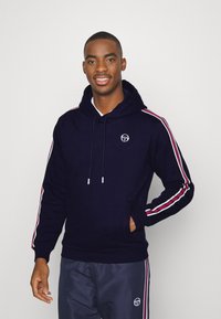 Felpa con cappuccio blu navy con strisce bianche e rosse sulle maniche, tasca a marsupio e logo sul petto. Tessuto morbido, vestibilità comoda.