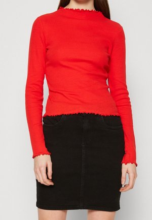 Rotes Langarmoberteil aus geripptem Strick mit einem Rüschensaum am Hals und an den Ärmelabschlüssen, kombiniert mit einem hoch taillierten schwarzen Jeansrock mit vorderen Taschen.