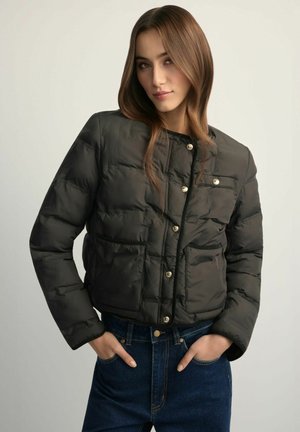 Czarna kurtka puchowa o krótkim kroju, zapinana na zatrzaski, z dwoma przednimi kieszeniami i fakturowanym wykończeniem. Zestawiona z ciemnoniebieskimi jeansami.