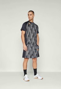 Meeste aktiivwear komplekt, mis sisaldab tumedat mustriga T-särki nurkade disainiga ja vastava spordiseeliku, mis on ühendatud valgete tossudega.