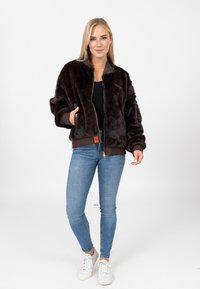 Bruine nep bont bomberjack met ribgebreide manchetten en zoom, gouden rits en zijzakken. G gedragen over een zwarte top en blauwe jeans.