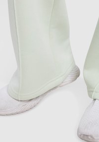 Vaaleanvihreät collegehousut, joissa on sileä pinta ja sivusaumat, yhdistettynä valkoisiin urheilukenkiin, joissa on verkkomateriaali päällä ja teksturoitu pohja.