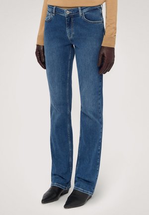 Blauwe spijkerbroek met een rechte pijp, voorzien van vijf zakken, een ritssluiting en een koperen knop. Gepaard met zwarte puntige laarzen.