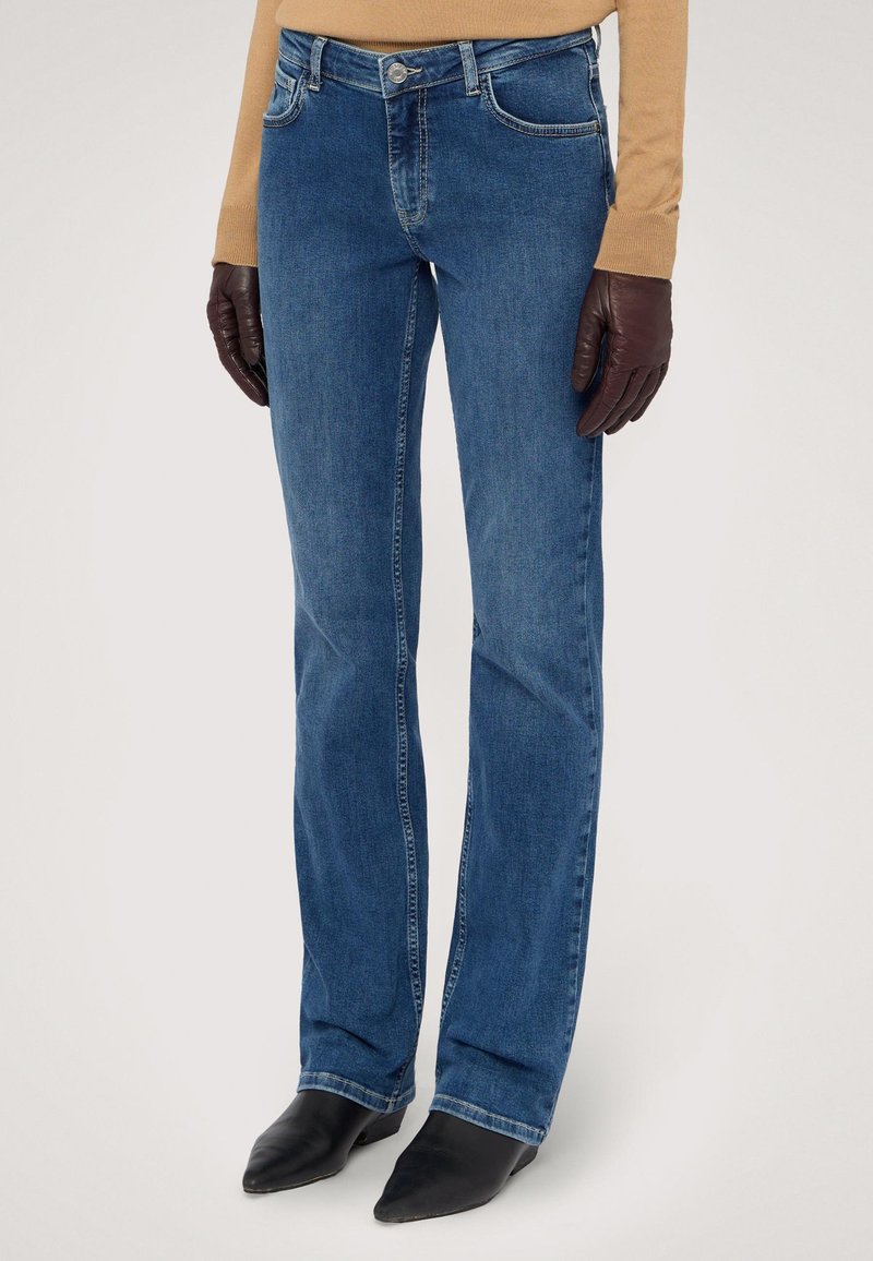 Vaqueros de denim azul con un corte recto, que cuentan con cinco bolsillos, una cremallera y un botón de latón. Combinados con botas negras de punta afilada.