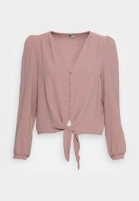 Blouse mauve à manches longues avec col en V, quatre boutons recouverts de tissu à l'avant, et nœud noué à la taille, en tissu texturé.