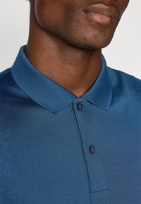 Blue polo shirt with a textured fabric, a structured collar, and two button placket. Features subtle color variations and a smooth finish.