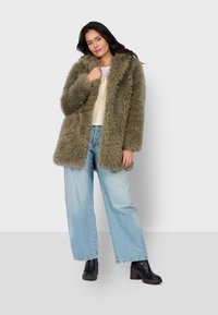 Faux fur coat in olive green, featuring a wide collar and front closure, paired with light blue wide-leg jeans and chunky black heeled boots.