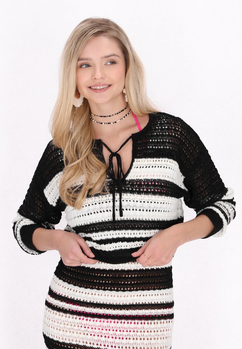Svartvit randig stickad topp med V-ringning och dragsko. Har en öppen vävstruktur och kontrasterande band.