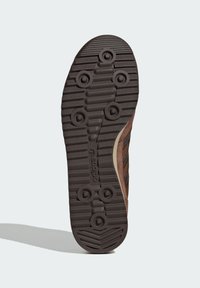 Brown rubber shoe sole with textured patterns and circular grip features; includes raised stripes and logo embossed on the side.